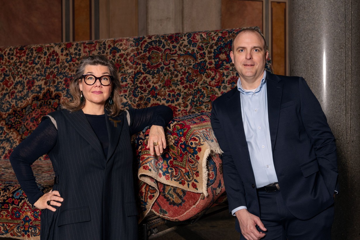 Zwei Personen lehnen an einem überdimensionalen Sofa das mit Teppichen bekleidet ist.