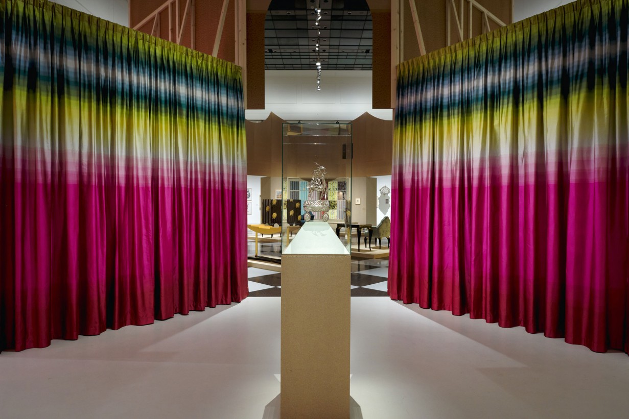 Ausstellungsraum mit Objekten, eingefasst von einem bunten Vorhang