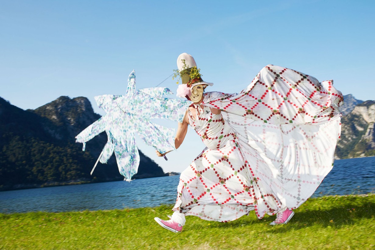 Verkleidete Person mit Maske und langem Mantel in weiß