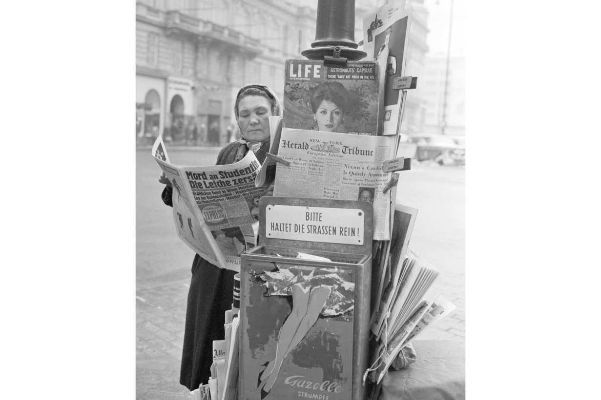 Black and white photograph of a woman at a newspaper stand