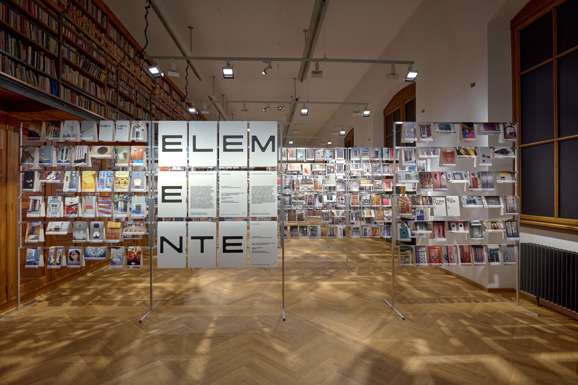 Viele Fotos mit Detailaufnahmen von Architektur hängen an an einem Gerüst in einem Ausstellungsraum.