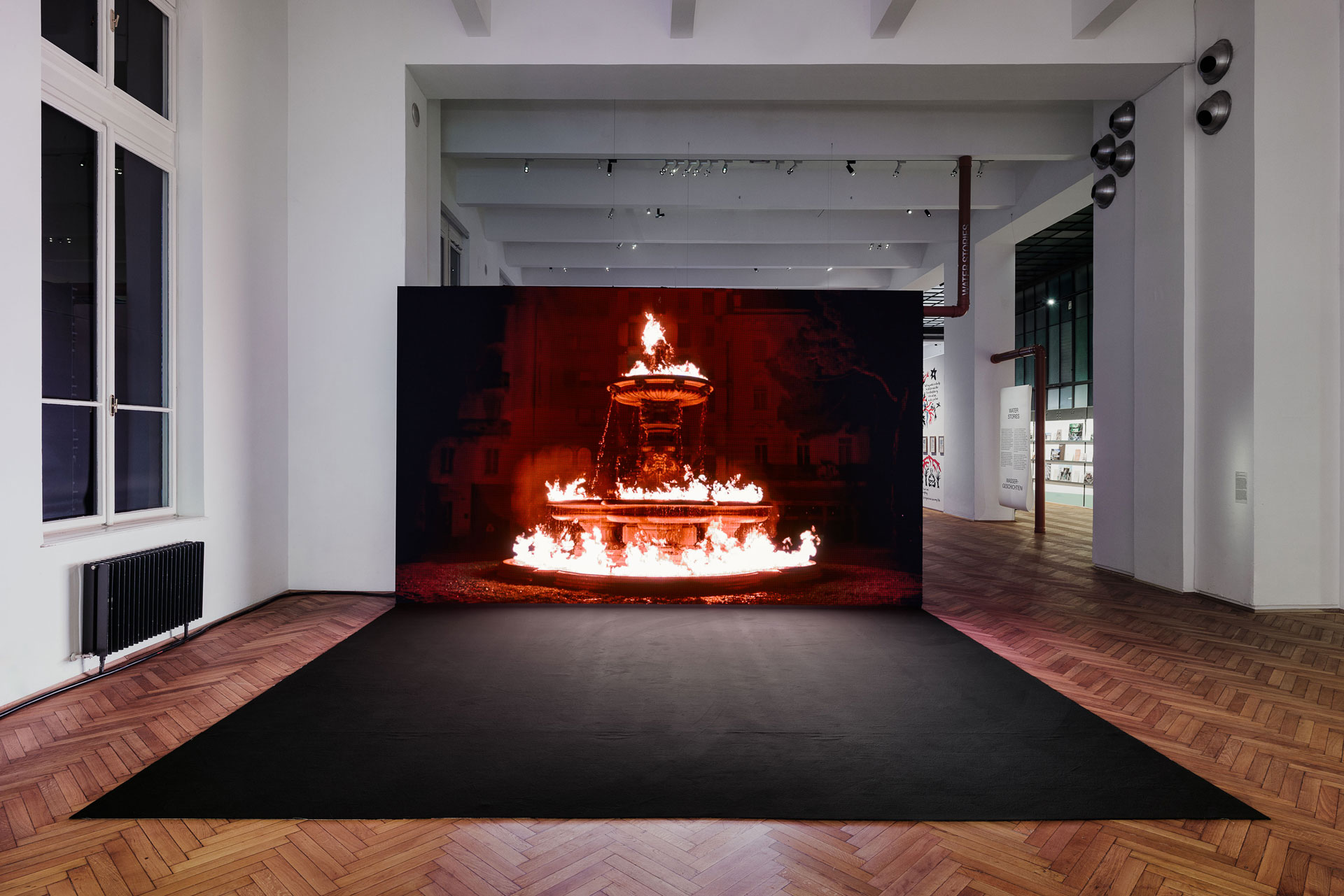Ausstellungshalle, Screen auf dem brennender Brunnen zu sehen ist